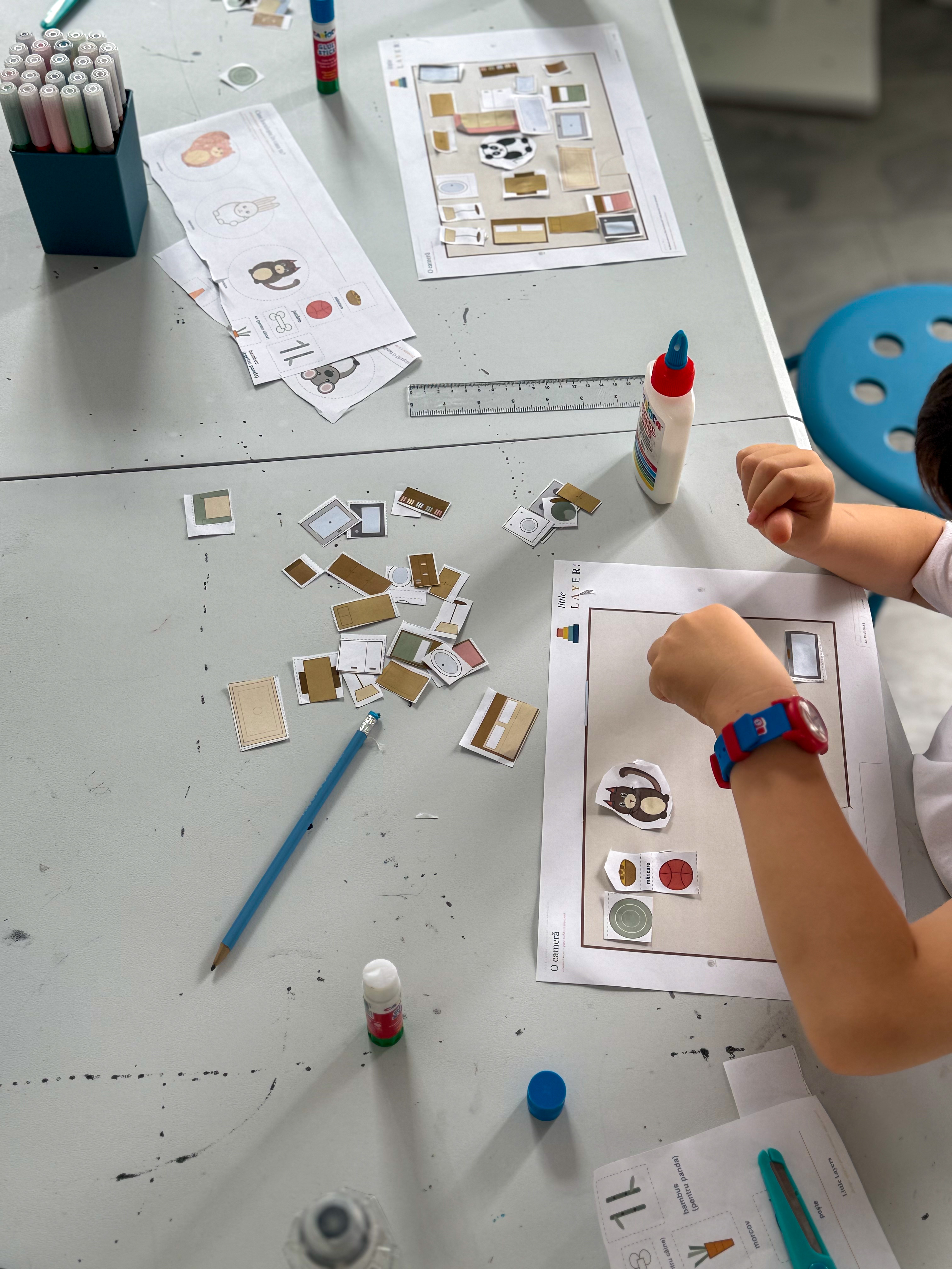 Un copil aranjând o cameră de hârtie cu mobilier decupat, văzut de sus