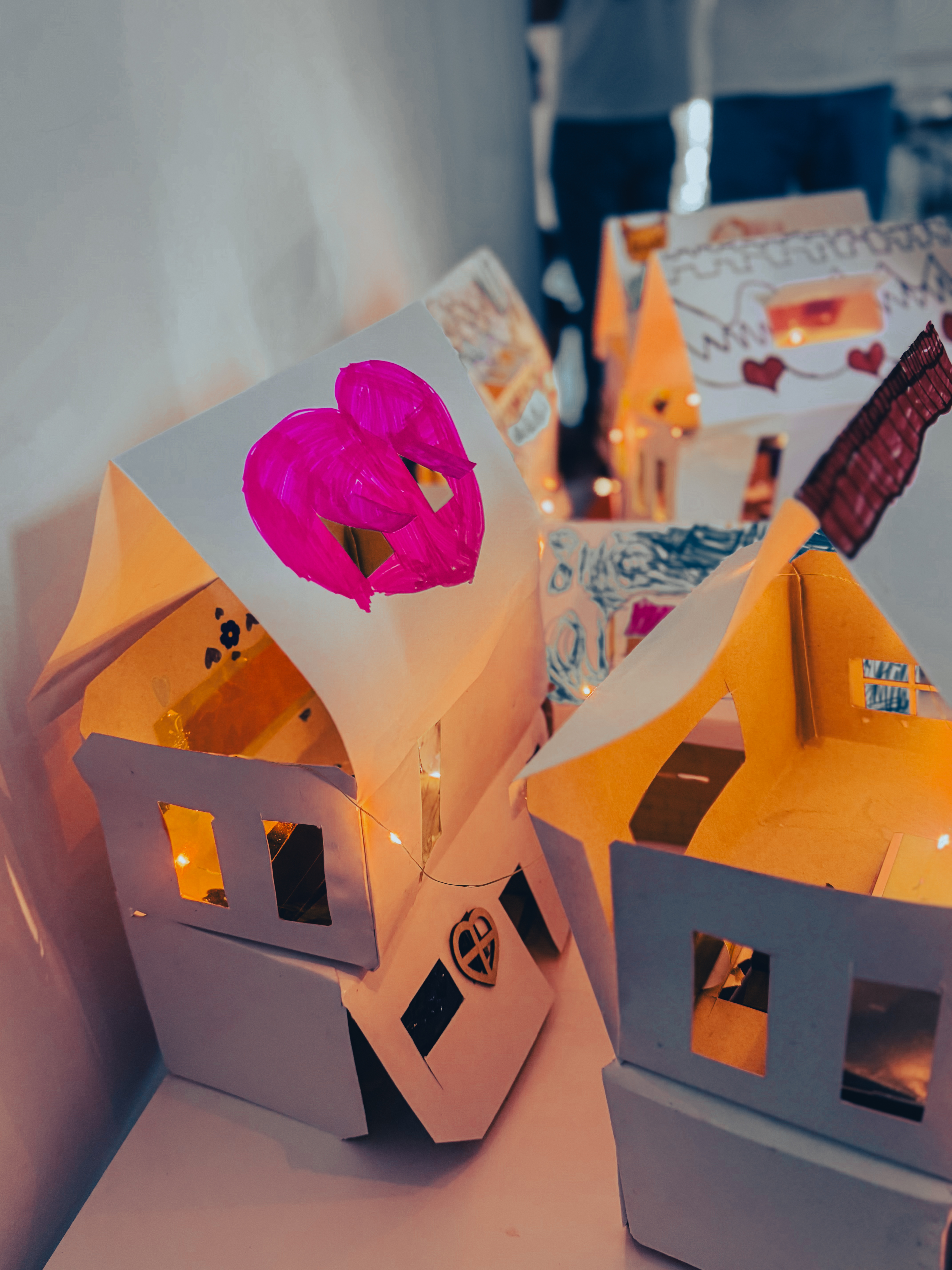Căsuțe de hârtie luminate din interior, cu o inimă desenată pe acoperiș — construite de copii la atelier