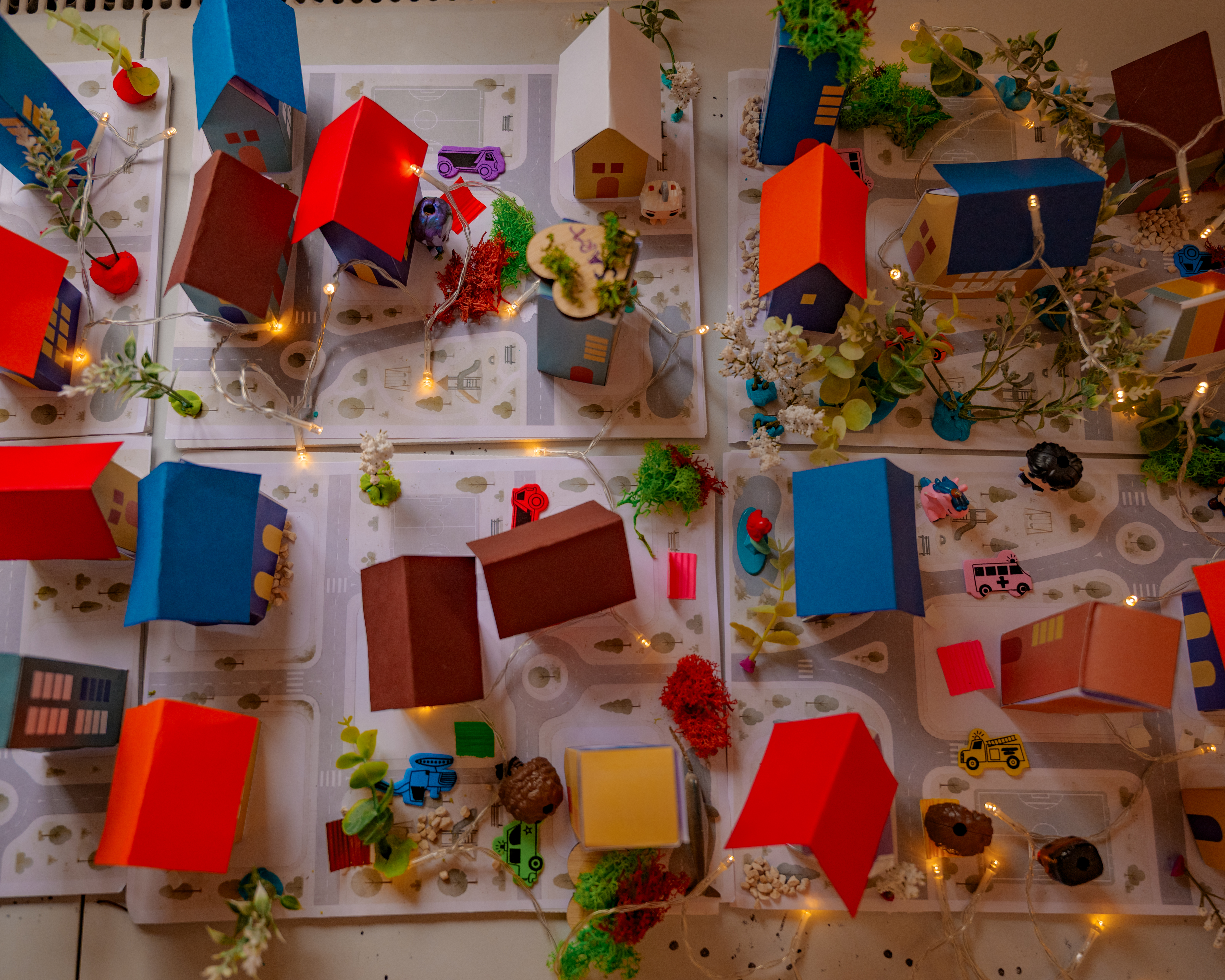 O fetiță lipește case de hârtie la masa de atelier, printre alte case colorate
