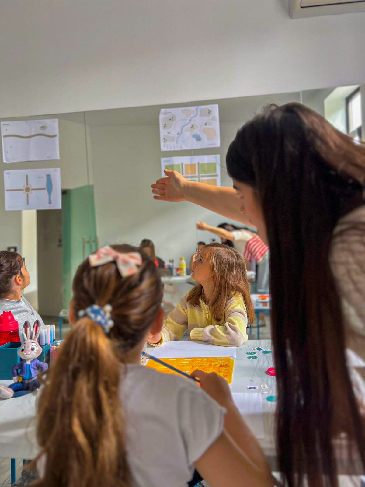 Copiii privesc planurile de pe perete, în timp ce Ioana le arată